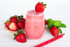 A strawberry smoothie in a short glass surrounded by bright red strawberries and two straws